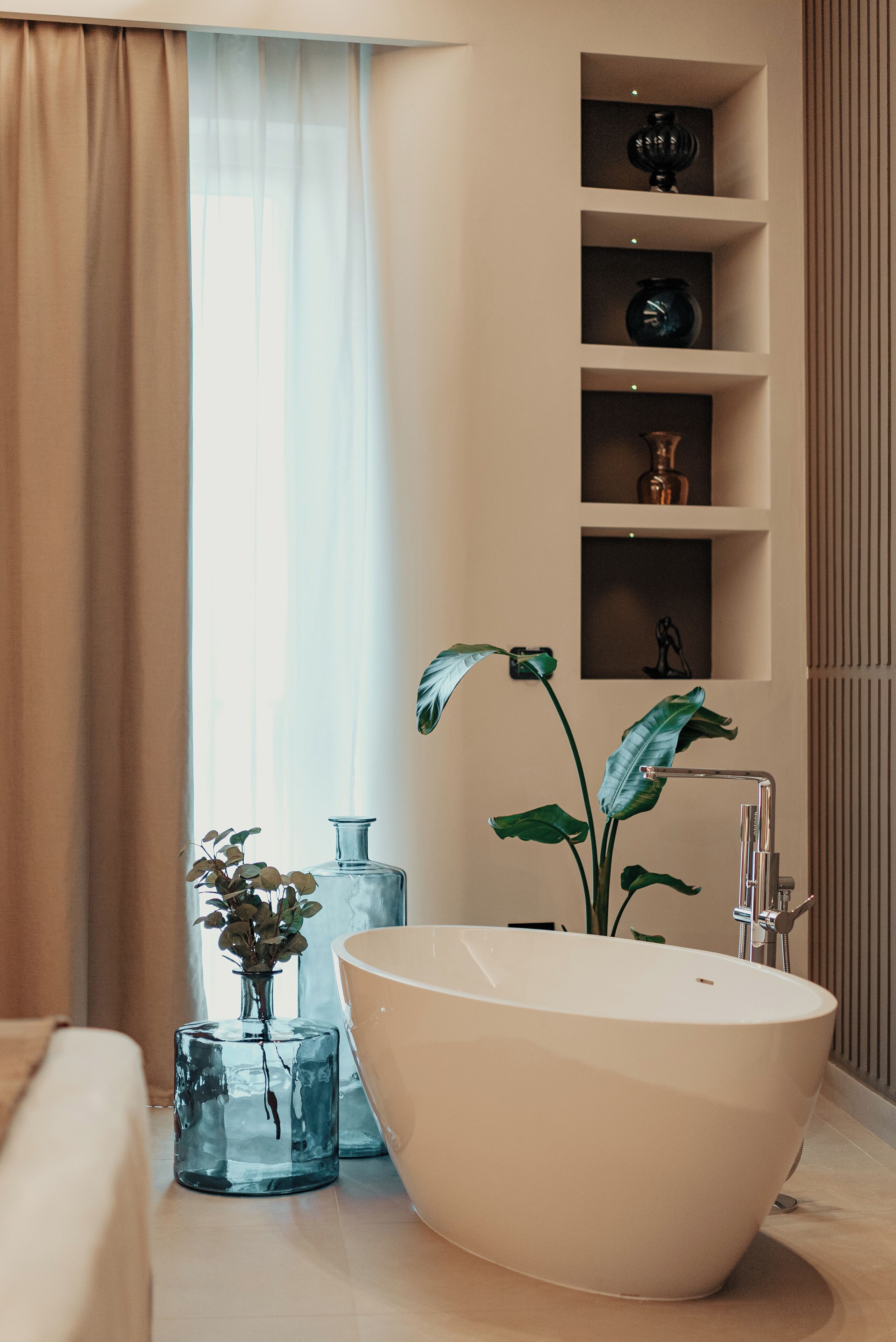 A modern bathroom with a freestanding bathtub, a glass vase with flowers, and a shelf with decorative items.