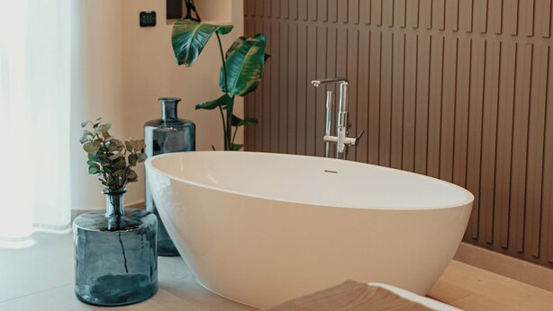 A modern bathroom with a freestanding bathtub, a wooden panel wall, and a shelf with decorative items.