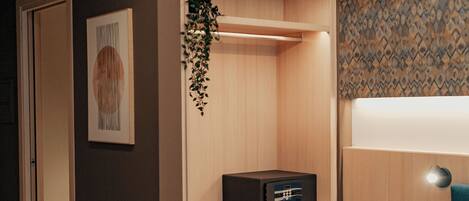 A hotel room with a bed, a wardrobe, a bedside table with a lamp, and a small plant.