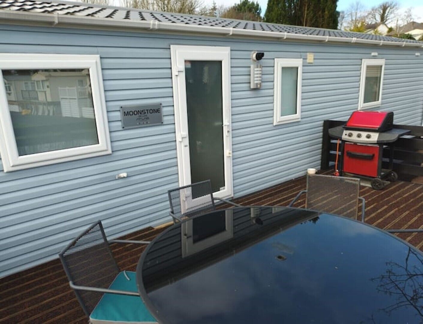 A blue mobile home with a sliding door, a small porch, and a barbecue grill.