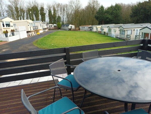 Um terraço com uma mesa redonda e cadeiras, com vista para uma área gramada com casas móveis.