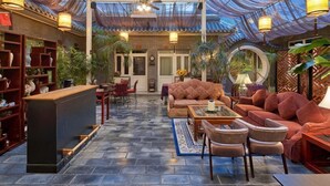 Un interior espacioso con techos altos, una zona de estar central con sofás y sillones, un área de bar con mostrador, y estanterías con objetos decorativos.