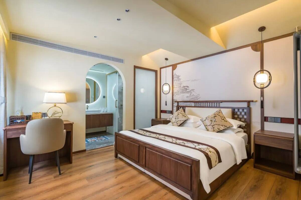 A hotel room with a large bed, a desk with a chair, and a mirror.