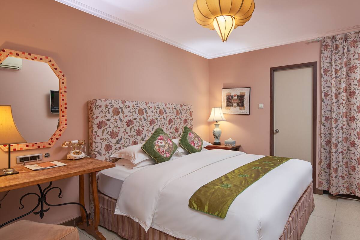 A hotel room with a bed, a desk with a lamp, a mirror, a television, and a door.