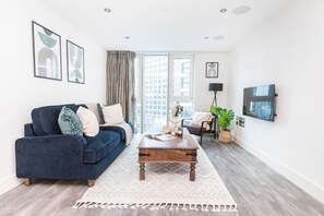 Un salon moderne avec un canapé bleu, une table basse en bois et une grande fenêtre agrémentée de rideaux.