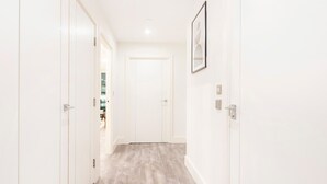 A hallway with white walls, a light wooden floor, and a door at the end. - Charming 2BR 2BA near Tower Bridge and Shoreditch (London)