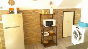 Une cuisine compacte équipée d’un réfrigérateur, d’un four à micro-ondes et d’un lave-linge. On peut voir une horloge et une petite étagère avec quelques objets accrochés au mur.