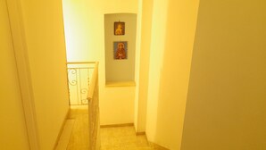 Un couloir étroit avec un escalier menant à un palier. Deux tableaux encadrés sont accrochés au mur.