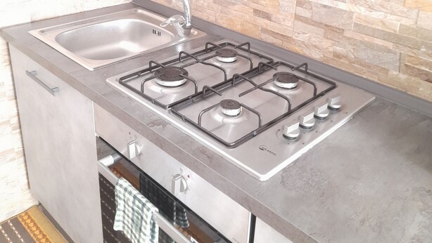 Une cuisine compacte équipée d’une cuisinière à gaz, d’un évier et d’un four encastré.
