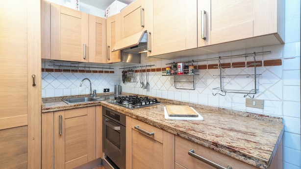 A kitchen with wooden cabinets, a granite countertop, a gas stove, and a stainless steel sink. - Laldiola (Olbia)