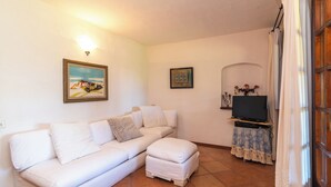A living room with a white sofa, a flat-screen TV, and a painting on the wall. - Laldiola (Olbia)