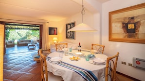 A dining area with a table set for four, a painting on the wall, and a view of the garden through an open door. - Laldiola (Olbia)