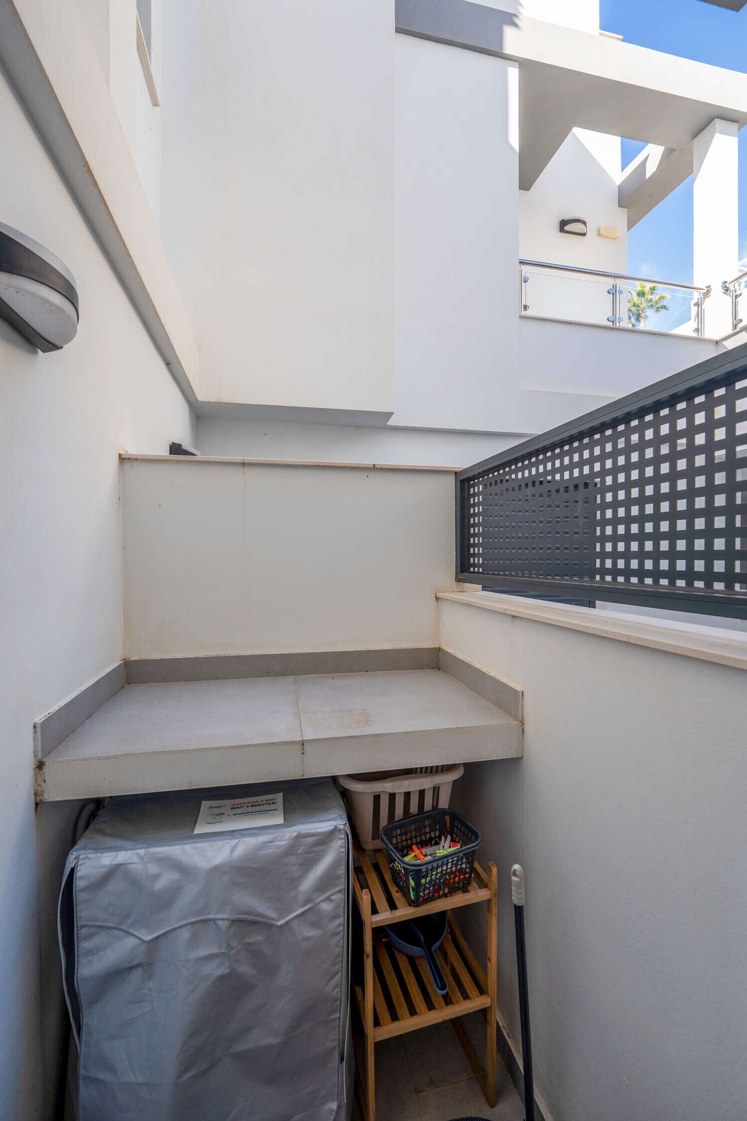 Ein kleiner, abgeschlossener Balkon mit einem Metallgitter, einem überdachten Gegenstand und einer Holzablage mit einem Korb.