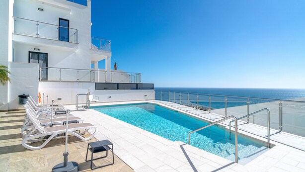 A modern pool area with clear blue water, sun loungers, and a view of the ocean.