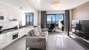 A modern apartment with a kitchen, living area, and balcony with a view of the sea.
