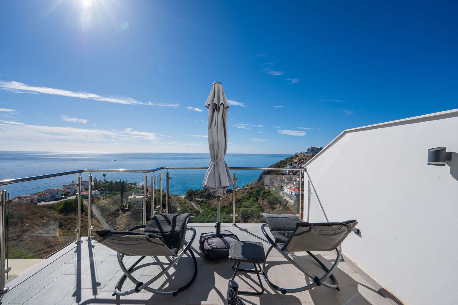 Un balcón con dos sillas y una mesa, con vistas a la costa.