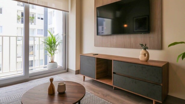 A modern living room with a large TV, a wooden cabinet, a round coffee table, and a potted plant. - w* | Marvelous 2BR with balcony in Miraflores (Lima)