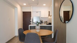 A modern dining area with a round table, four grey chairs, a vase with a plant, a coffee machine, and a mirror on the wall. - w* | Marvelous 2BR with balcony in Miraflores (Lima)
