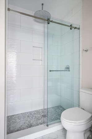 Une salle de bain moderne avec une douche à parois de verre, des murs recouverts de carreaux blancs et des toilettes.
