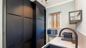 Een moderne keuken met zwarte kastjes, een roestvrijstalen spoelbak, een magnetron en een raam met zonwering.