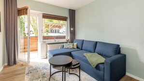 Een moderne woonkamer met een blauwe modulaire bank, een klein rond tafeltje en uitzicht op een houten terras en auto's.