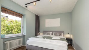 Een slaapkamer met een bed, een radiator, een raam met zonwering, een nachtkastje en een wandlamp.