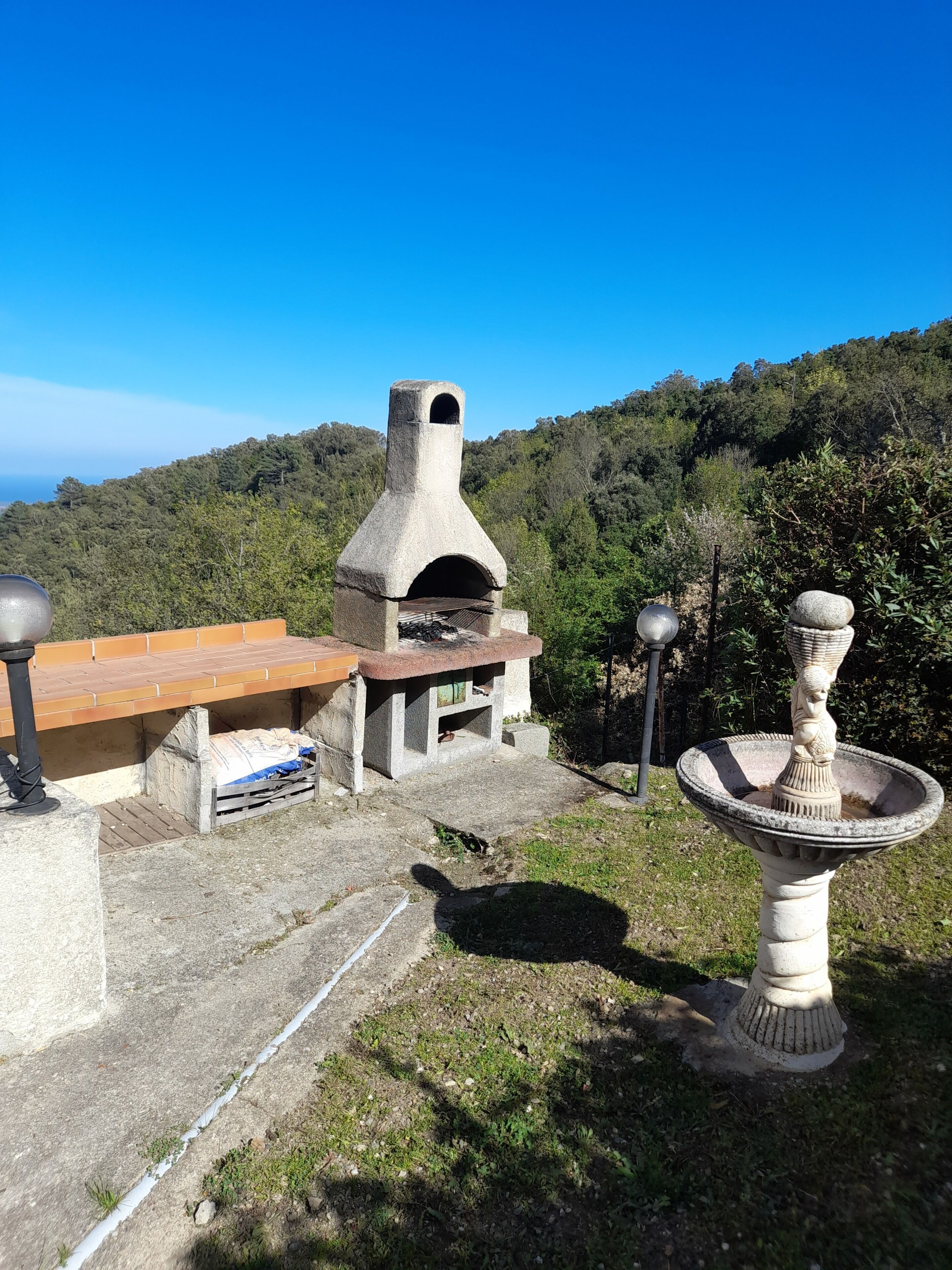 A stone outdoor kitchen with a chimney, a wooden table, and a stone fountain.