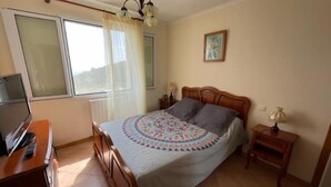 Une chambre à coucher avec un lit, une télévision, une fenêtre avec des rideaux, une table de chevet et une lampe.