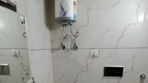 A bathroom with a white sink, a toilet, and a water heater mounted on the wall. - Hotel Mannat International (New Delhi)