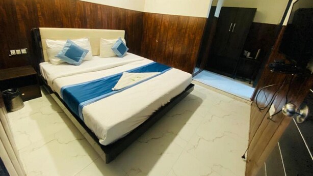 A hotel room with a bed, a wooden wardrobe, a small table, and an air conditioning unit on the wall. - Hotel Mannat International (New Delhi)