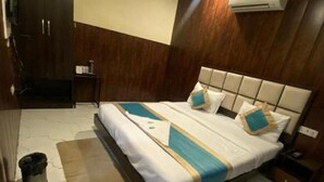 A hotel room with a bed, a ceiling fan, an air conditioning unit, a wooden wardrobe, and a small table. - Hotel Mannat International (New Delhi)