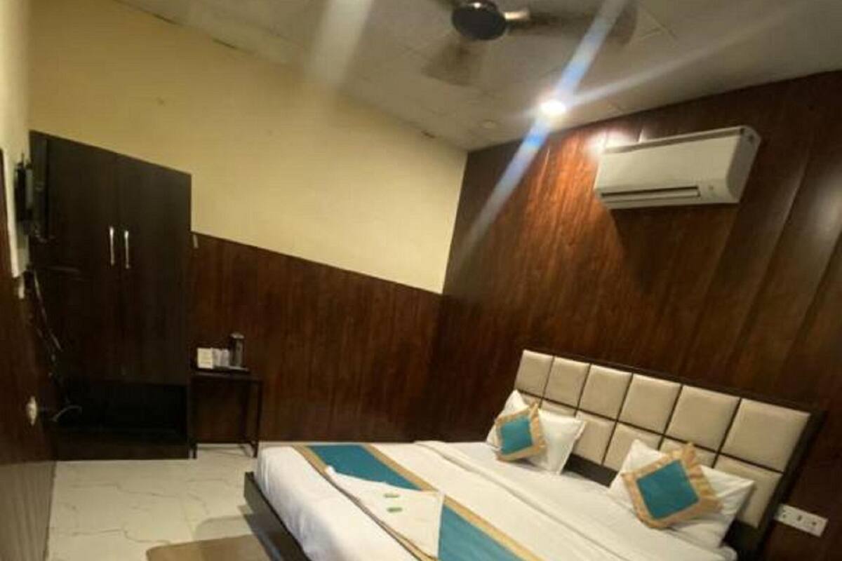 Une chambre d’hôtel avec un lit, un ventilateur de plafond, un appareil de climatisation, une armoire en bois et une petite table.