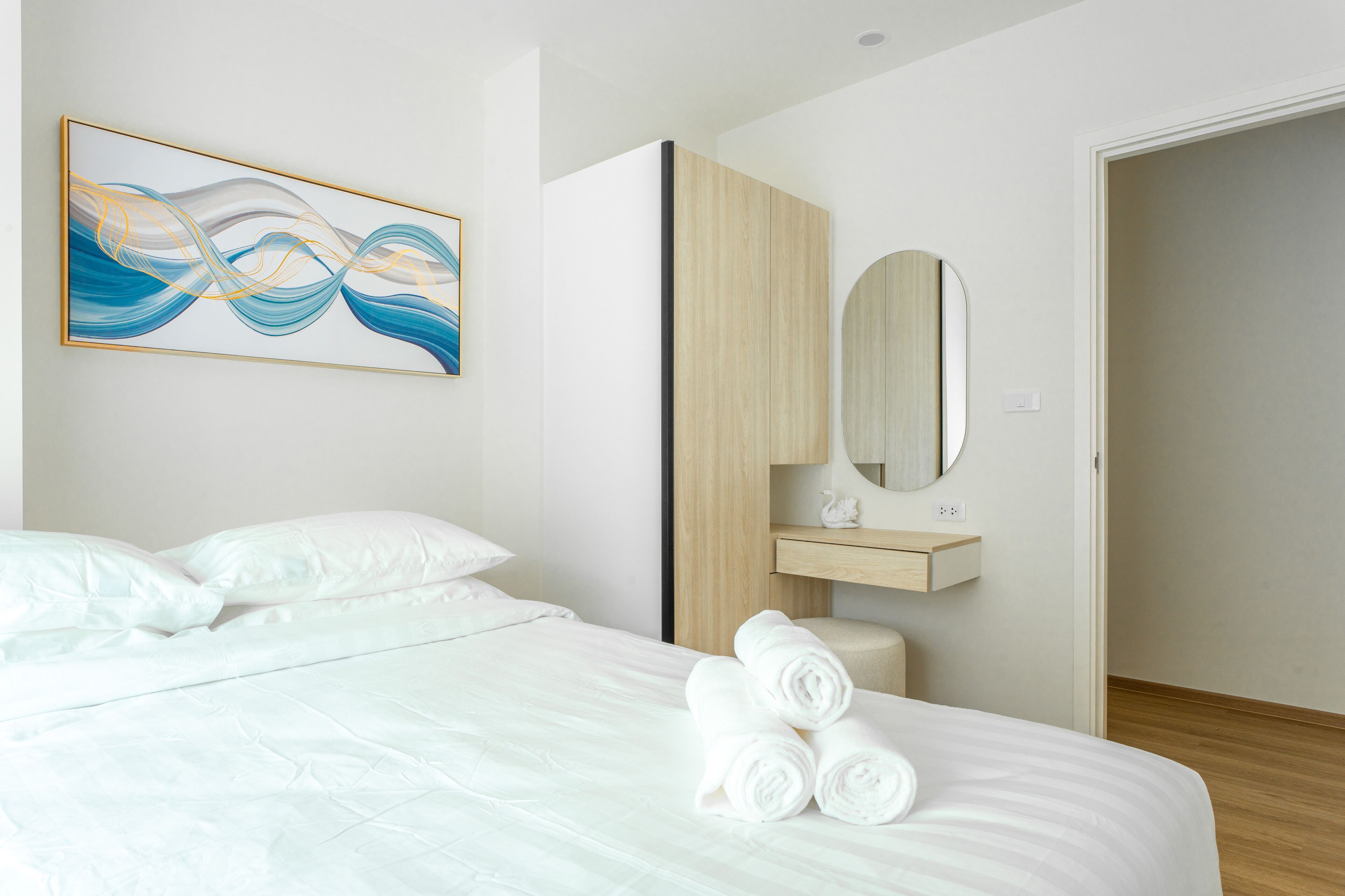 Une chambre d’hôtel moderne avec un lit soigneusement fait, une œuvre d’art accrochée au mur, une armoire en bois et un miroir.