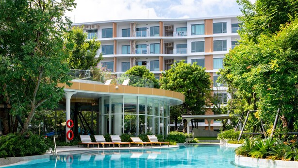 A swimming pool with lounge chairs, surrounded by greenery and a modern building with multiple floors and balconies. - Phyll Phuket by NLA (Wichit)