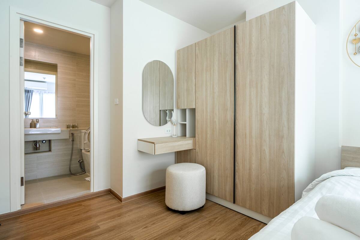 A modern bedroom with a wooden floor, a large bed, a bedside table, a mirror, and a wardrobe.