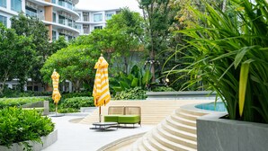 A modern outdoor area with a pool, green seating, and yellow-striped umbrellas. - Phyll Phuket by NLA (Wichit)