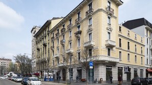 A multi-story building with a yellow facade, multiple balconies, and storefronts on the ground floor. - Easylife - Elegance in the Isola district (Milano)