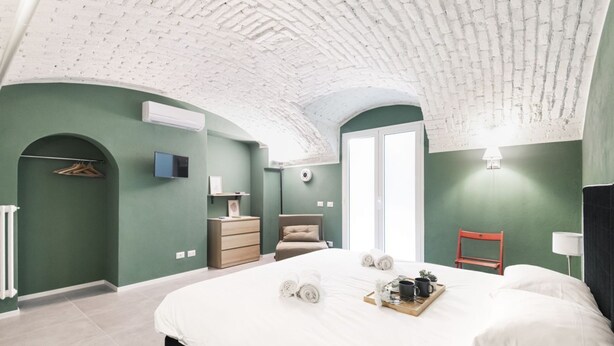 A bedroom with a curved ceiling, a bed with rolled towels, a bedside table with a lamp, and a chair. - Easylife - Elegance in the Isola district (Milano)