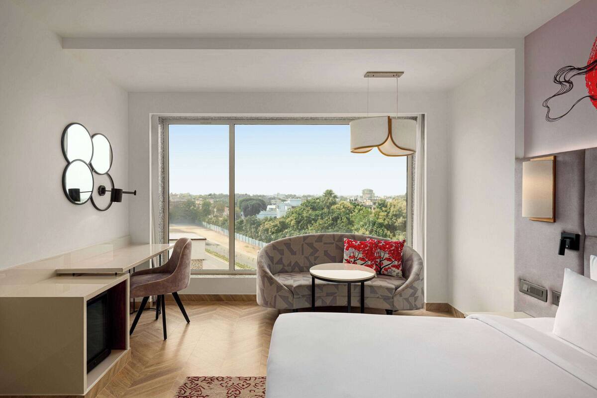 Ein modernes Hotelzimmer mit einem großen Bett, einem Schreibtisch, einer Sitzecke und Blick auf die Stadt.