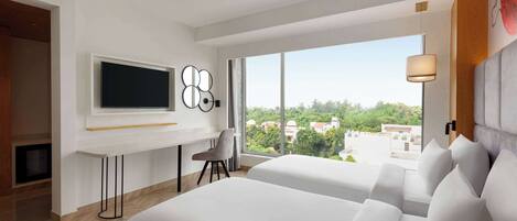 A modern hotel room with a large bed, a desk with a flat-screen TV, a chair, and a large window offering a city view.