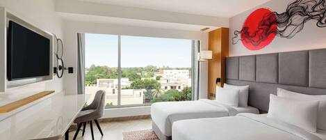 A hotel room with two beds, a desk, a TV, and a large window offering a city view.