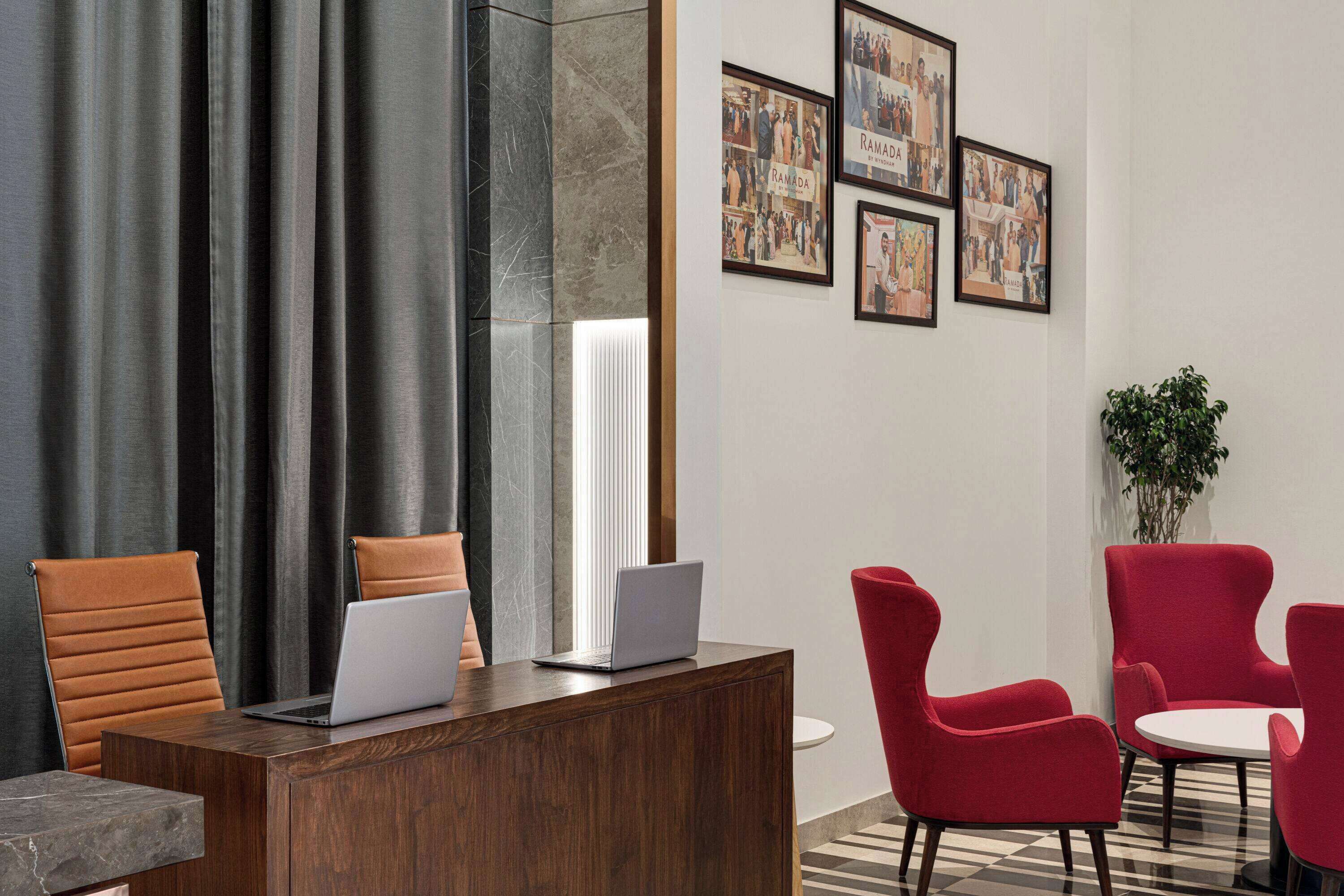 Un espace d’accueil avec un bureau en bois, un ordinateur portable, des chaises rouges et des tableaux encadrés accrochés au mur.