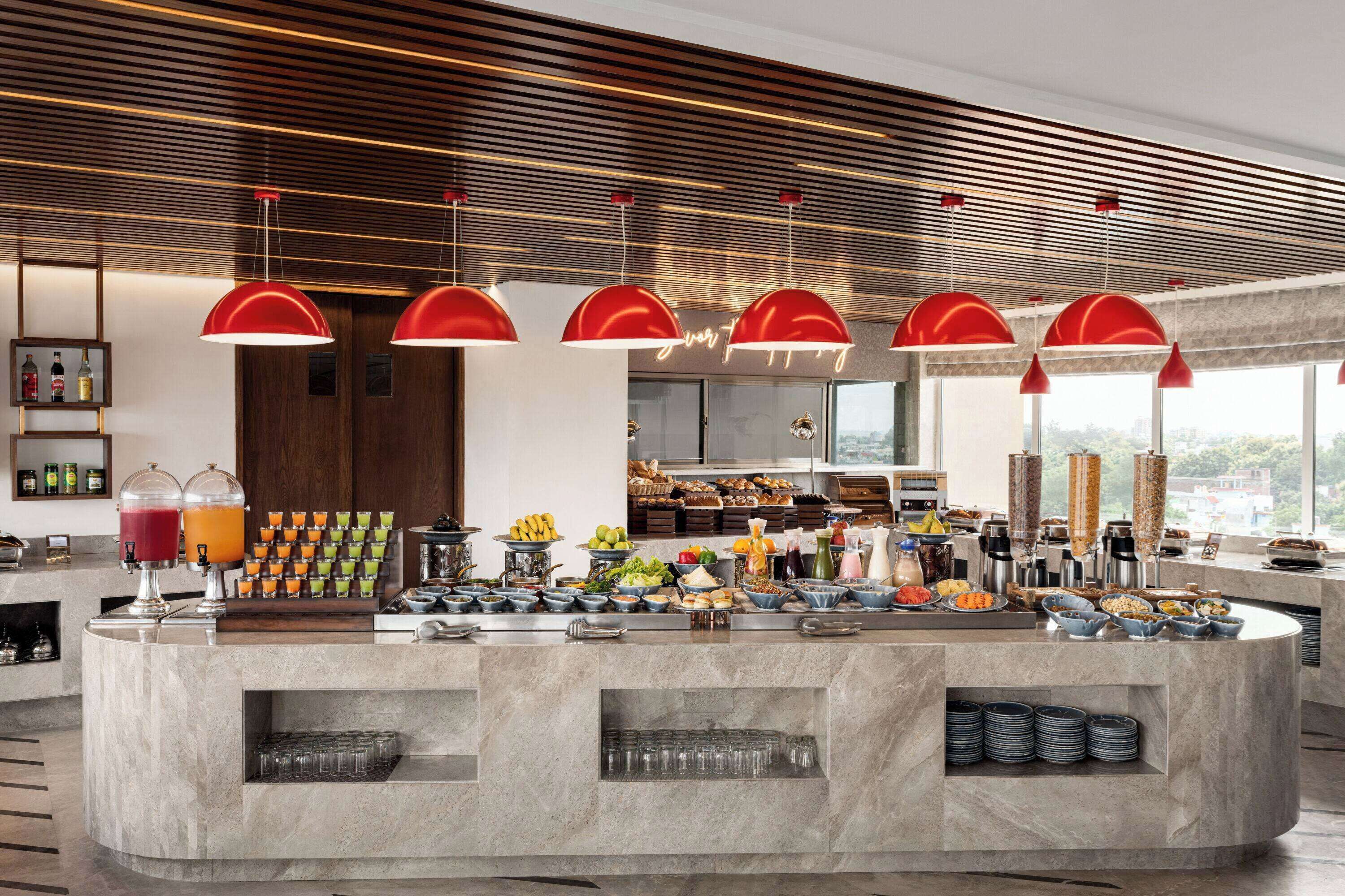 Una barra de desayuno moderna con diversas opciones de comida y bebida, como frutas, pasteles y refrescos.