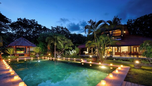 A swimming pool with candles around the edge, surrounded by lush greenery and a gazebo.