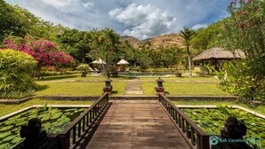 A wooden bridge leading to a pool surrounded by lush greenery and a mountain backdrop.