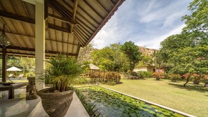 A covered outdoor area with a pond, potted plants, and a grassy lawn.