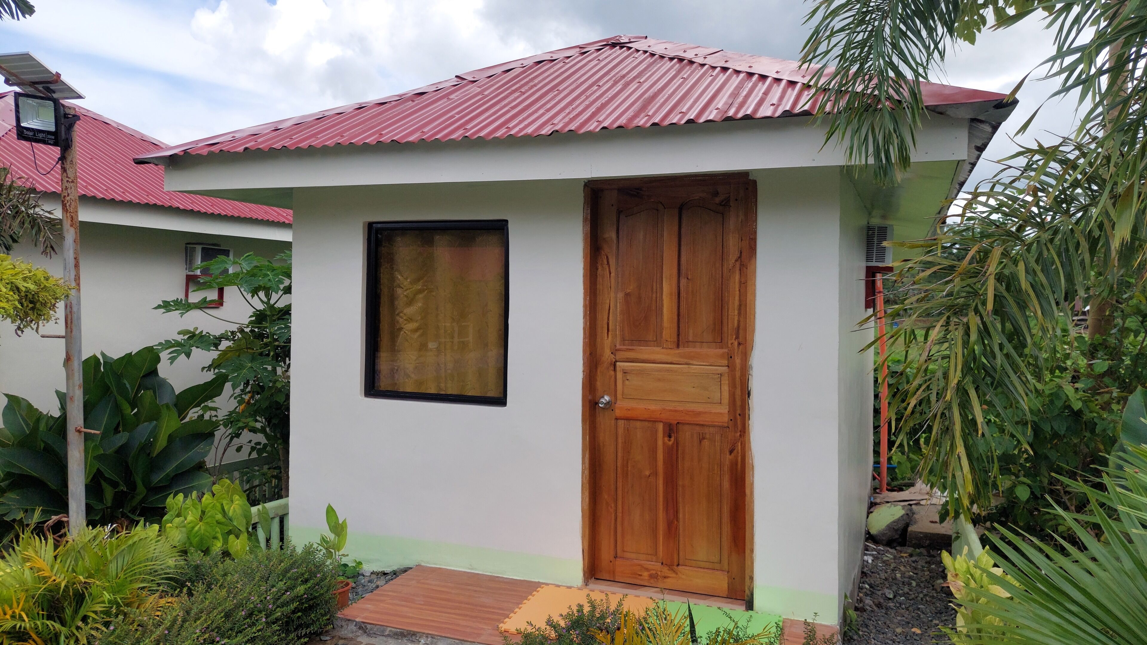 Un pequeño edificio con techo de láminas rojas, una puerta de madera y una ventana.