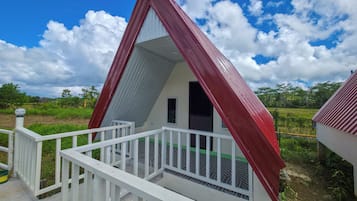 Um pequeno edifício triangular com telhado vermelho e paredes brancas, apresentando uma varanda com grade branca.