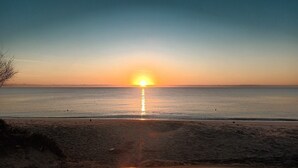 Ranta auringonlaskun aikaan, tyyni vesi ja kirkas taivas.