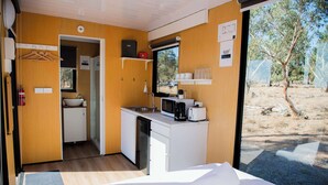 A compact room with a bed, a kitchenette, a sink, and a window with a view of trees.